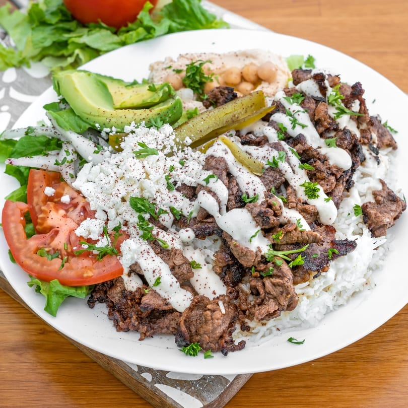 A Falafel California beef shawarma plate with rice, hummus, avocado, feta, and vegetables.