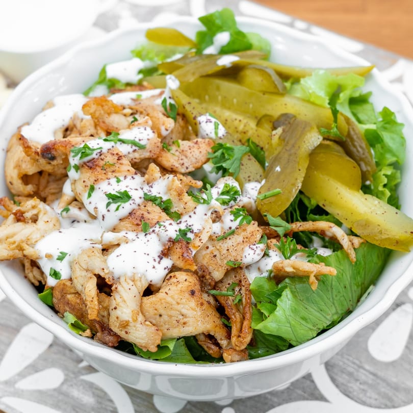 Falafel California's chicken shawarma salad with lettuce, pickles, and white sauce in a bowl.