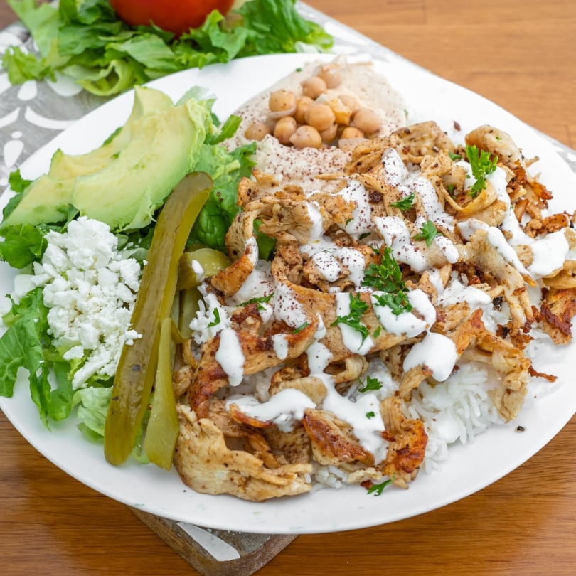Falafel California's chicken shawarma plate with rice, hummus, salad, avocado, feta, and pickles.