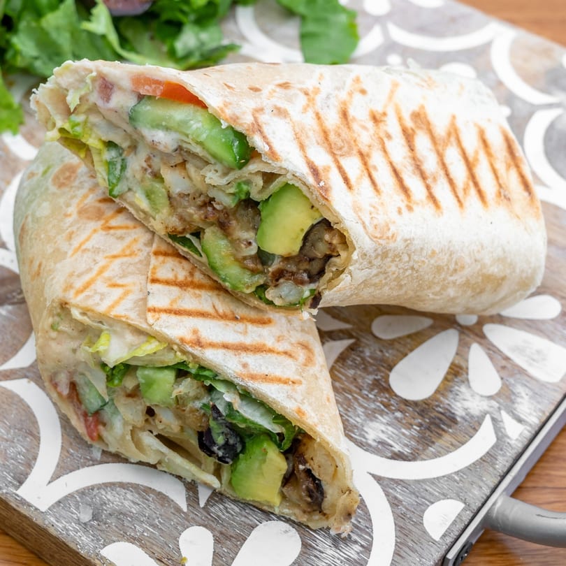 Two halves of a Falafel California wrap filled with avocado, lettuce, and falafel on a wooden board.